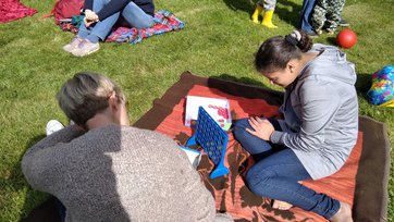 Frau und Mädchen spielen Vier-Gewinnt auf einer Decke im Park
